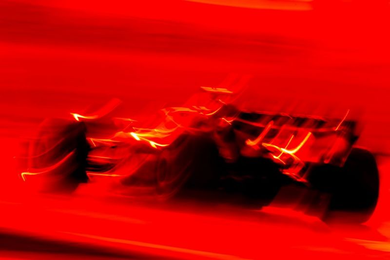 A Formula One race car captured at low shutterspeed and in full red colour tone, producing blurred lines that give an artistic look to match the speed of the car.