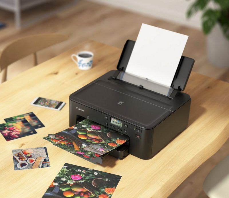 Op een houten tafel staat een Canon PIXMA TS705-printer waarmee afbeeldingen van fruit en bloemen worden geprint.