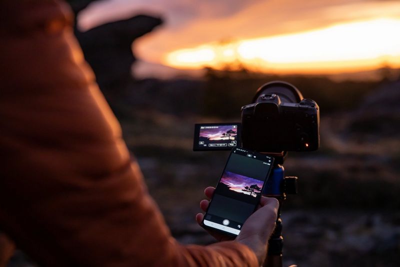Фотограф со штативом стоит на каменистой земле, направив камеру в сторону ночного звездного неба.