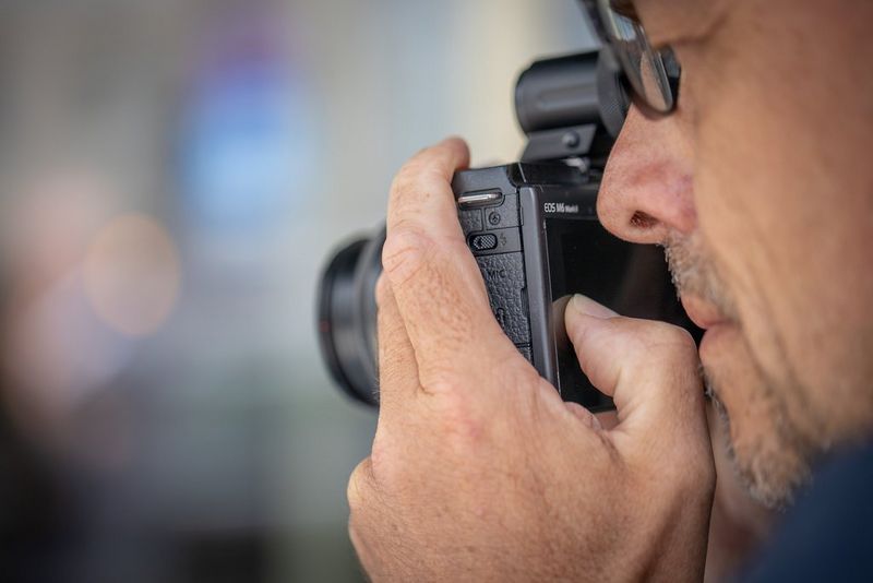 Мужчина смотрит в видоискатель камеры Canon EOS M6 Mark II.