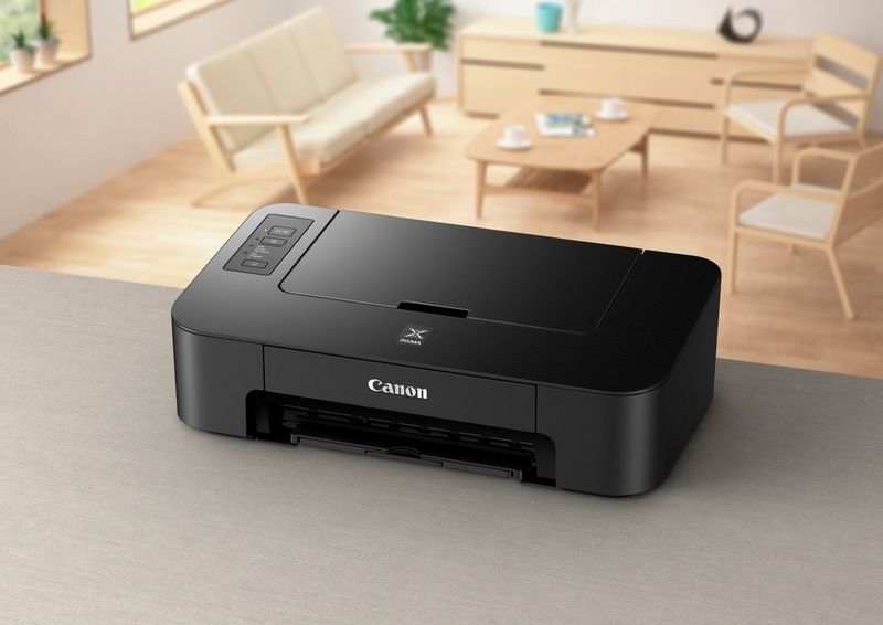 A Canon PIXMA printer on a dark grey work surface. In the background a small wooden table and three chairs can be seen. 