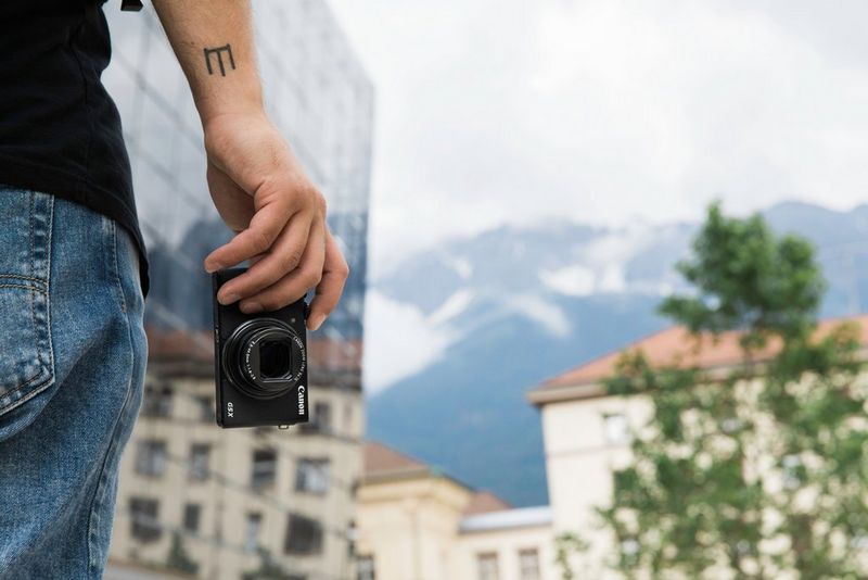 A Canon PowerShot G5 X Mark II is held lightly in a man's hand by his side.