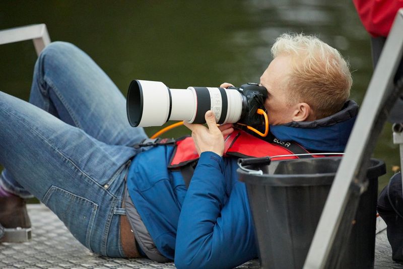 Een fotograaf in een spijkerbroek en een blauwe jas leunt naar achteren om een foto te maken met een Canon-camera en een RF 70-200mm F.2.8L IS USM-lens.