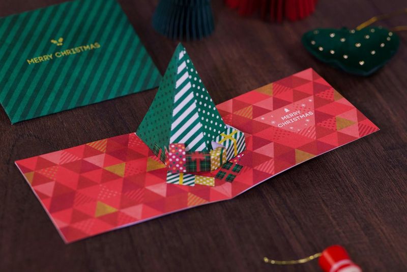 A completed Christmas pop-up card from Canon Creative Park featuring a triangular green-and-white striped Christmas tree on a red patterned background.