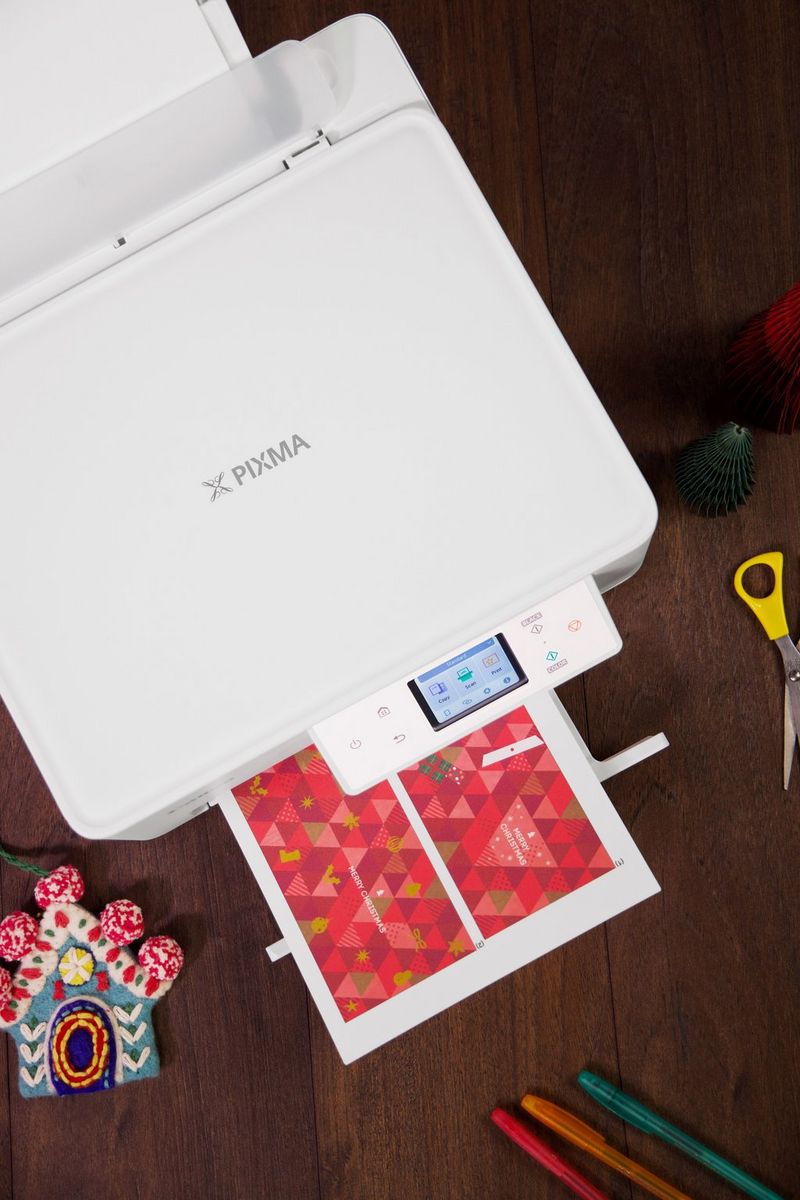 A Canon PIXMA printer is printing a festive red sheet with a holiday-themed design.