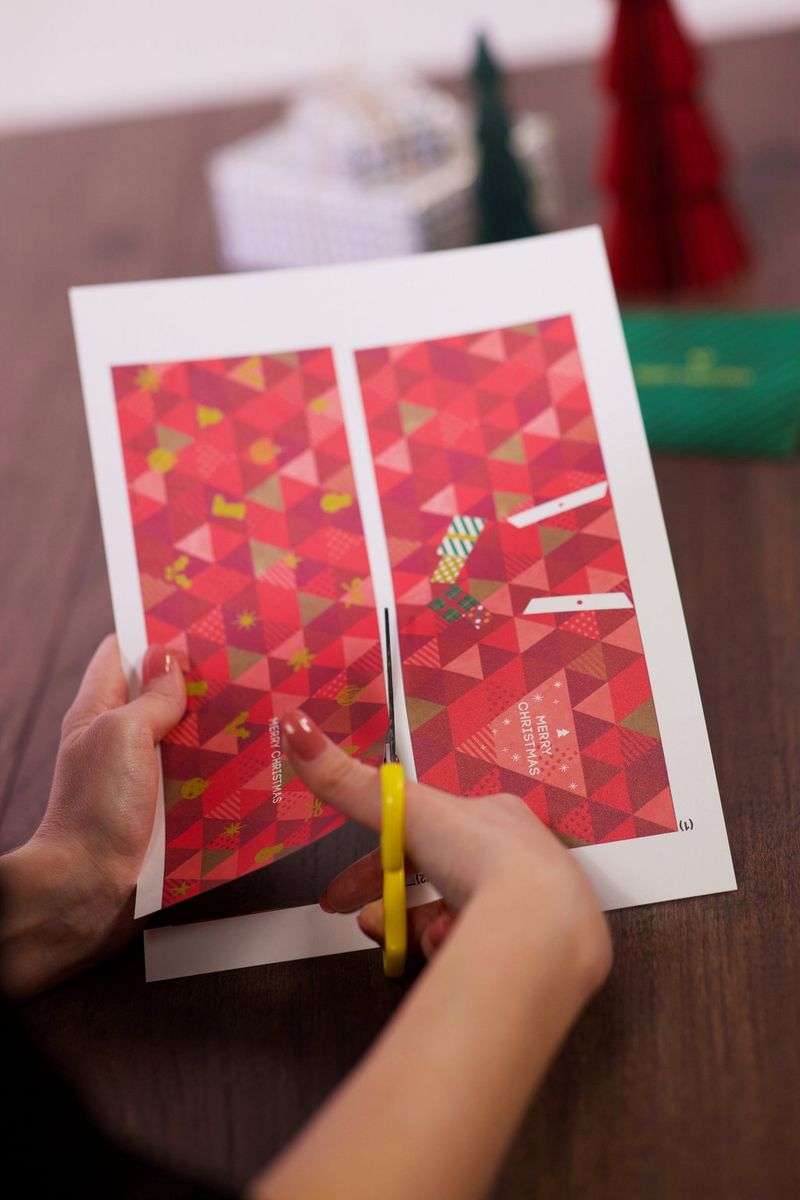 יד גוזרת בזהירות לאורך הקווים של גיליון מודפס בנושא החגים ליצירת כרטיס קופץ.