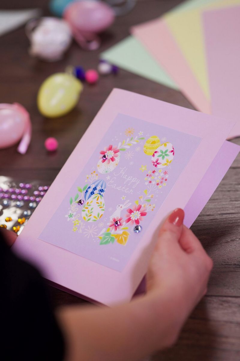 יד אוחזת בכרטיס חג פסחא בצבעי פסטל, הכולל איורי ארנבת וביצי פסחא.