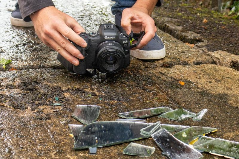 A camera is held close to the ground, aiming at a group of overlapping shards of mirror.