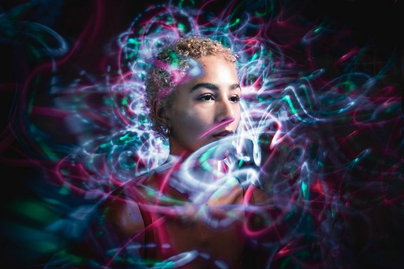 Multiple colourful light trails weave around the head and torso of a model, against a black background.