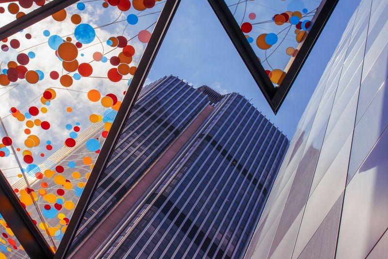 A street photography shot of the side of a skyscraper shot from below, with colourful glass covering one side.