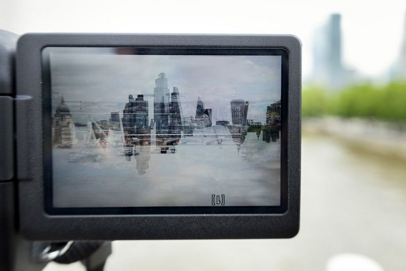 An upside-down LCD screen on a Canon camera showing a double exposure of buildings seemingly suspended in the sky. 
