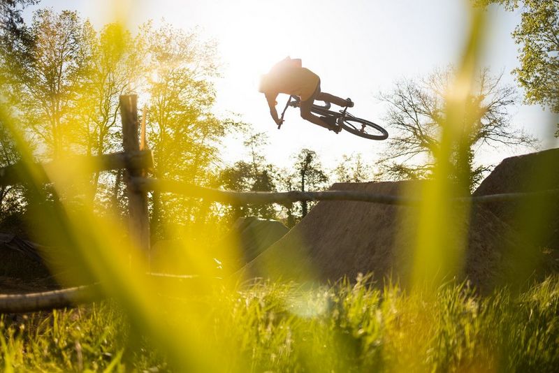 Gorski kolesar med skokom v sončnem vremenu s travo v ospredju prizora.