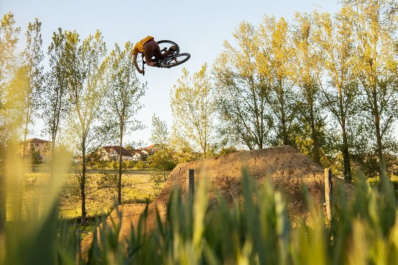 Gorski kolesar med visokim skokom, katerega najvišja točka je poravnana z bližnjo gozdno mejo.