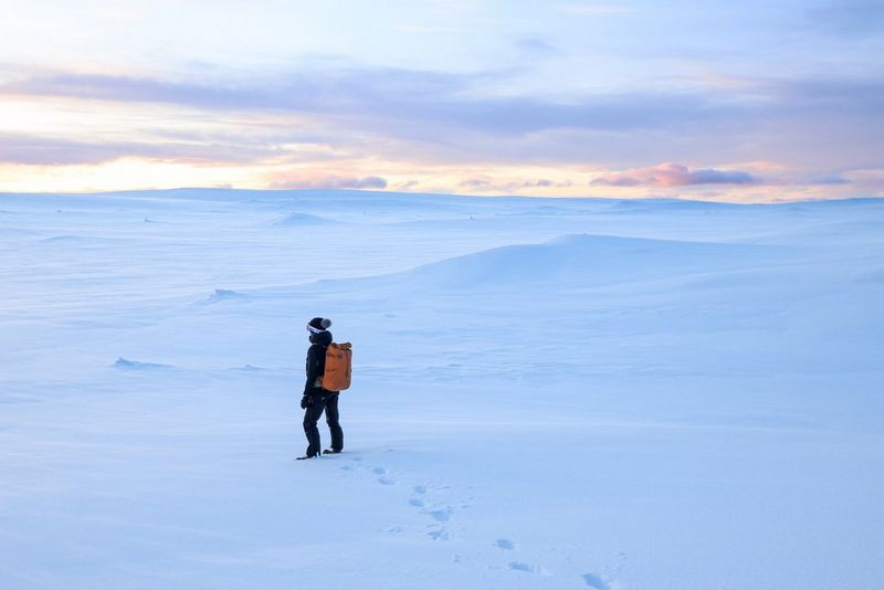 Donna con uno zaino arancione che cammina in un paesaggio innevato.