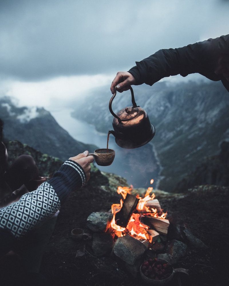 Dvije osobe uživaju u kavi na otvorenom uz malu logorsku vatru. U pozadini je veličanstvena dolina.