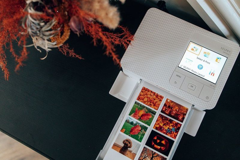 A sheet of autumn-themed images emerging from a Canon compact printer.