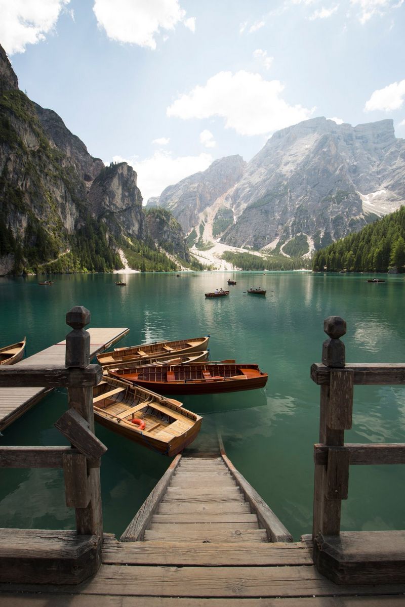 Lago di Braies in Zuid-Tirol (Italië), met uitzicht over de Dolomieten op de achtergrond. Op de voorgrond zijn houten treden en talloze kleine boten zichtbaar.