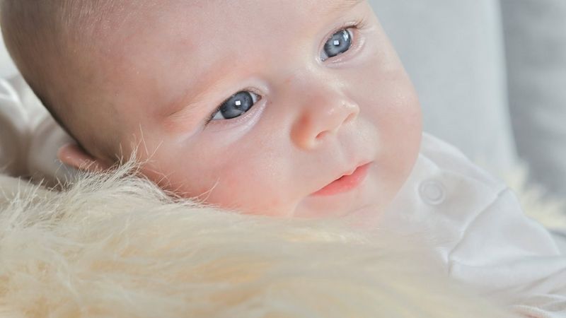 A close-cropped photo taken on a Canon EOS R10 of a baby raising its head from a fluffy blanket and looking intently to one side.