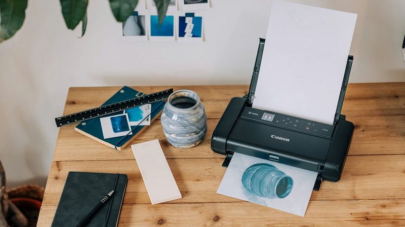 Een Canon PIXMA TR150 print een foto van een kleine blauwe vaas, die ook naast de printer staat.