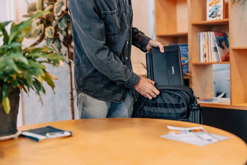 Мужчина кладет принтер Canon PIXMA TR150 в черный рюкзак.