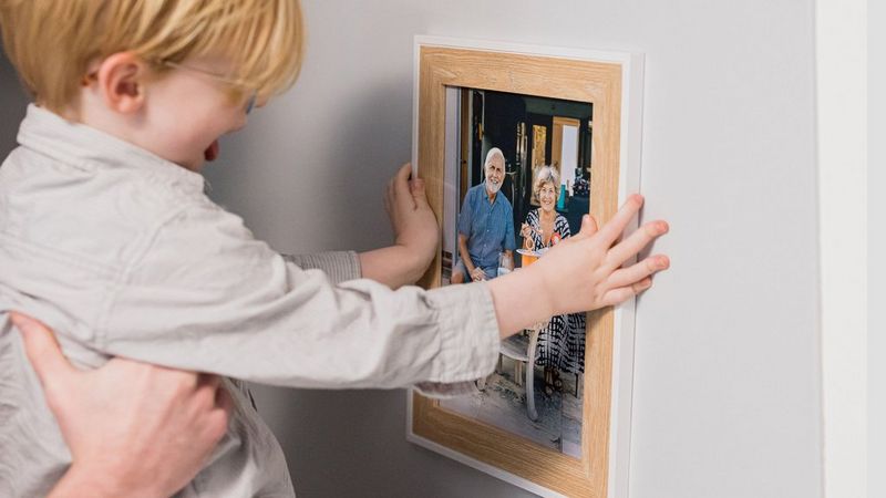 Ruky držiace dieťa, aby umiestnilo na stenu zarámovanú fotografiu.