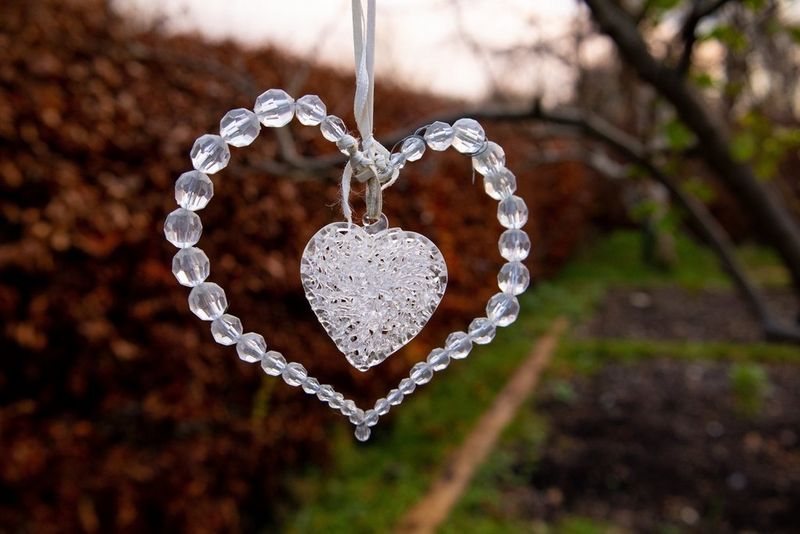 Садовое украшение в форме сердца из стеклянных бусин перед осенней живой изгородью.