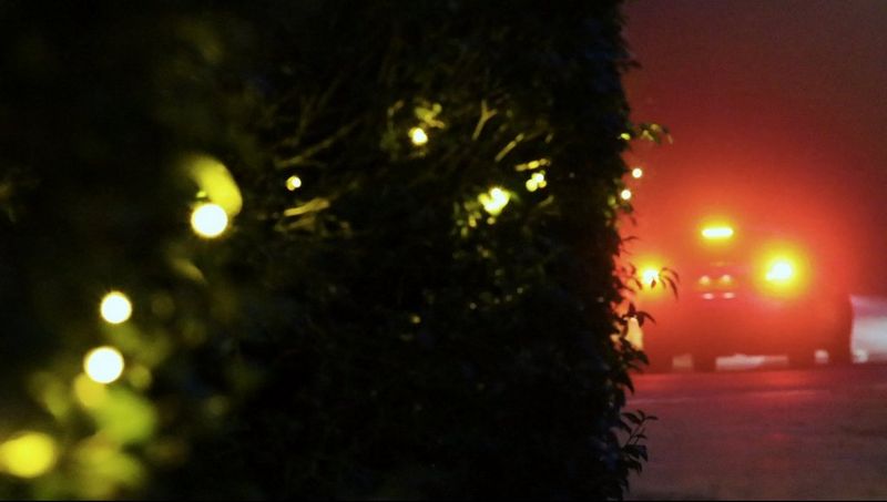 Twinkling Christmas tree lights in the foreground and a car's rear lights in the background are all out of focus.