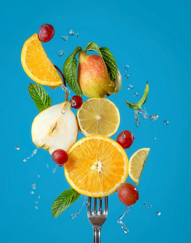An assortment of fruits arranged as if in mid-air, skewered onto a fork, with a bright blue background. 