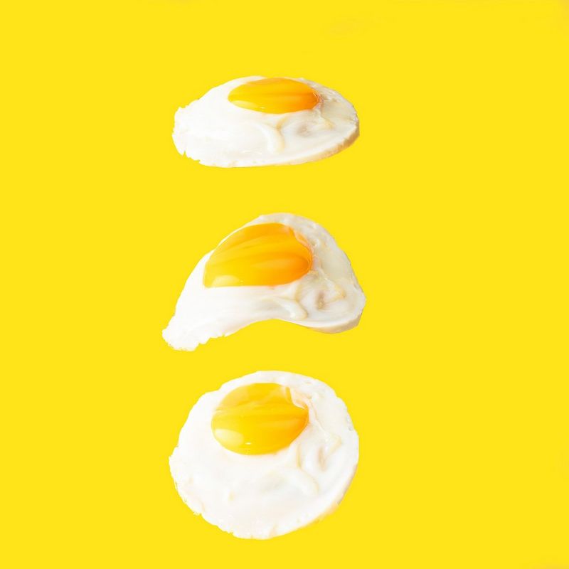 Three fried eggs, appearing to float in a line on a yellow background. 