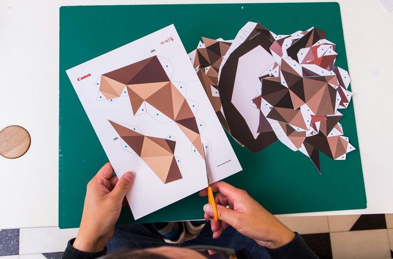 A person uses a pair of scissors to cut a dinosaur papercraft template downloaded from Canon Creative Park.