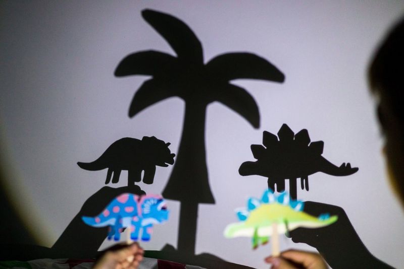 Two people play with assembled Canon Creative Park dinosaur puppets as they cast shadows on the wall behind.