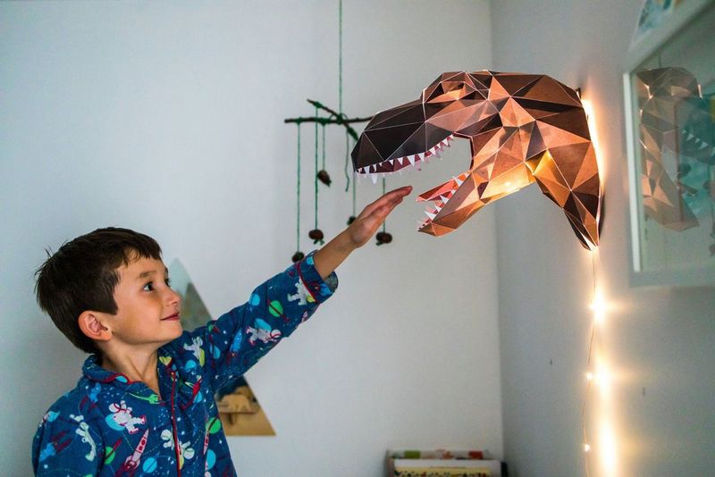 A child reaches his hand out to the assembled dinosaur night light, downloaded from Canon Creative Park, which hangs on a wall. 