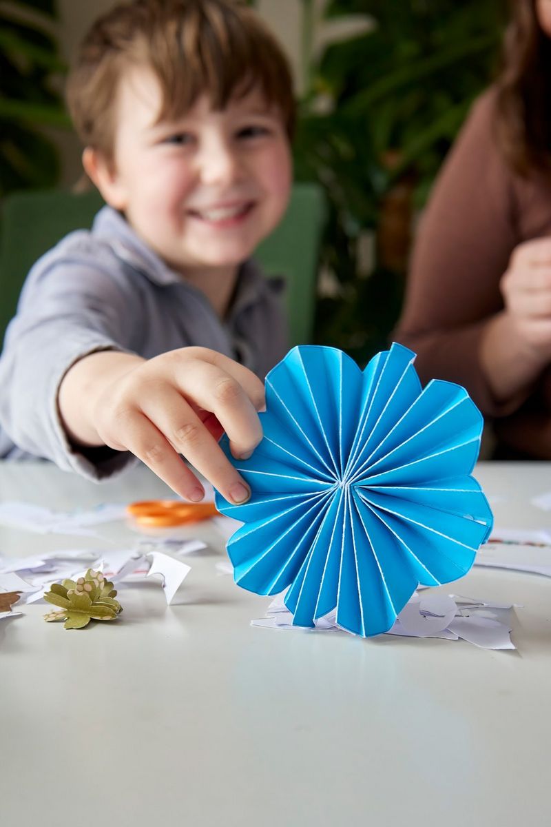 A young boy smiles at the camera while holding a blue paper flower created from a Canon Creative Park template.