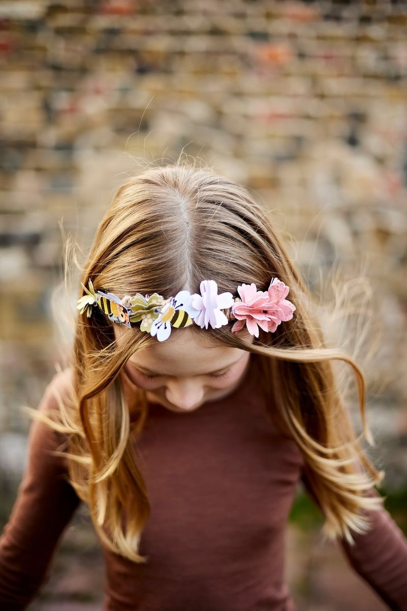 A young girl looks down at the ground to show her paper flower crown to the camera.