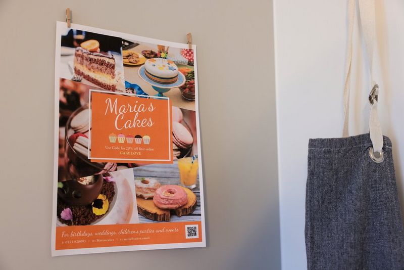 Een poster voor een bedrijf genaamd Maria's Cakes is bevestigd aan een muur, met het bedrijfslogo in het midden en foto's van cakes eromheen.
