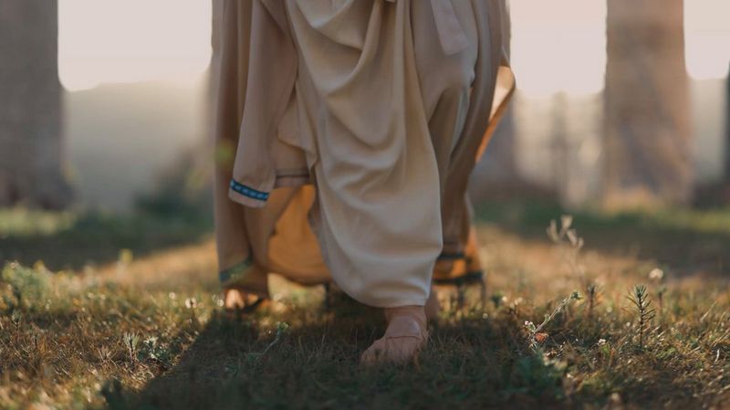O persoană îmbrăcată într-o robă lungă, plimbându-se în faţa unei ruine antice.
