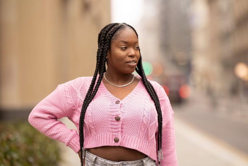 דיוקן של אישה עם צמות ארוכות, לבושה בעליונית ורודה בגזרה מקוצרת עם איזון לבן חם יותר.