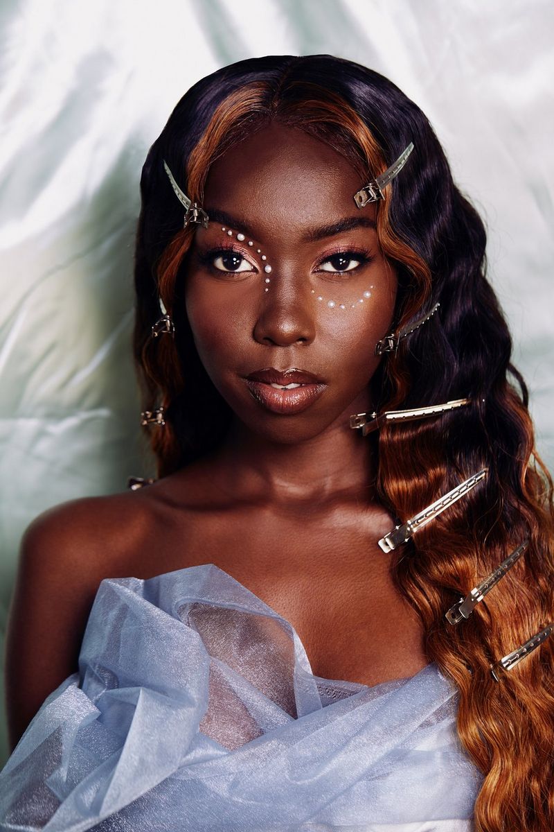 דיוקן אופנתי של אישה לבושה בשמלה בצבע תכלת. שיערה גלי ומלא בקליפסים.