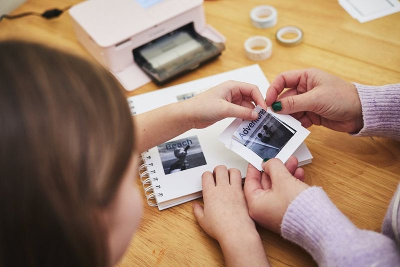 A child peels a photo from Canon sticker paper – printed using a Canon SELPHY CP1500 – while another person holds it.