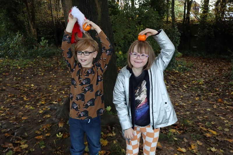Zwei Kinder halten Orangen über ihre Köpfe. Das Kind auf der linken Seite trägt zudem eine rote Weihnachtsmütze. Aufgenommen mit einer Canon EOS R100.
