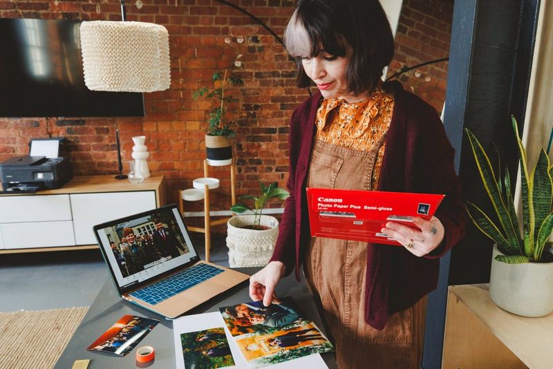 Une sélection de photos de mariage posée devant un ordinateur portable ouvert, tandis qu'une femme examine une photo qui vient juste de sortir de l'imprimante.