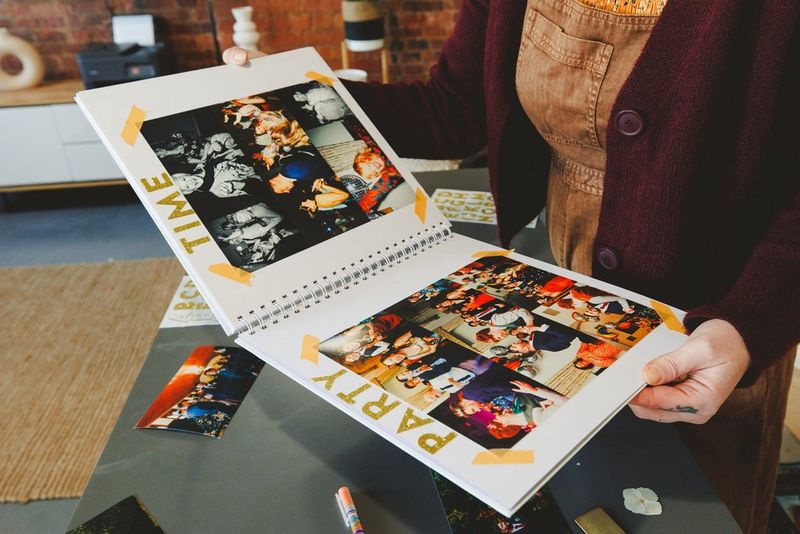 A person holding a homemade wedding album filled with photos of the reception. Glittering gold letters spelling PARTY TIME have been stuck at the top.