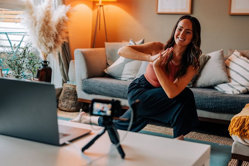 Een jonge vrouw in een felgekleurde top doet yoga in haar huiskamer terwijl een Canon PowerShot G7 X Mark III-camera haar bewegingen filmt.