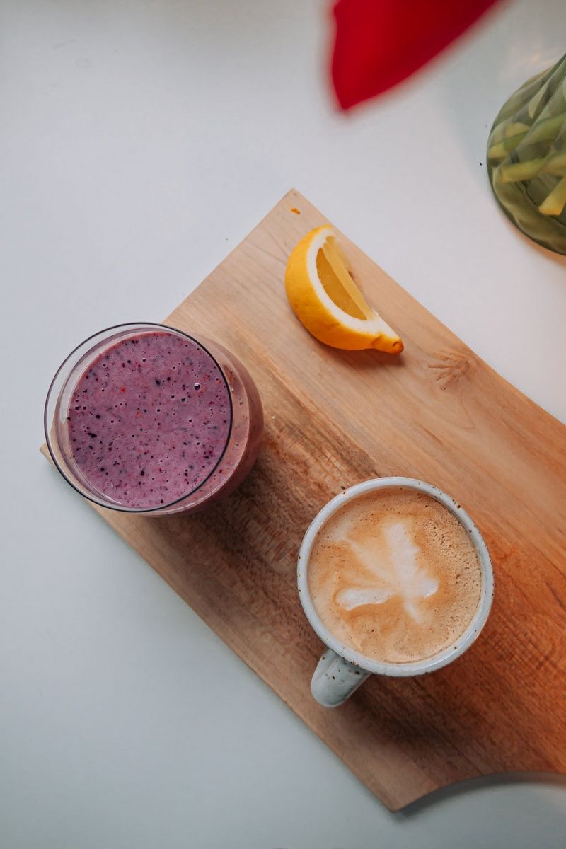 Een opname van bovenaf van een fruitshake, een koffie met schuim en een schijfje sinaasappel op een snijplank.