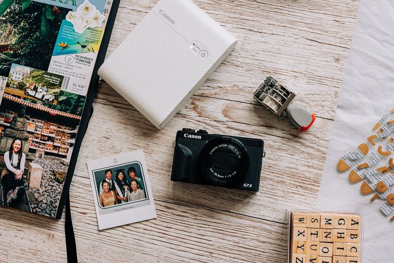Een Canon PowerShot G7 X Mark III op een tafelblad met een SELPHY Square QX10 en een scrapbook.