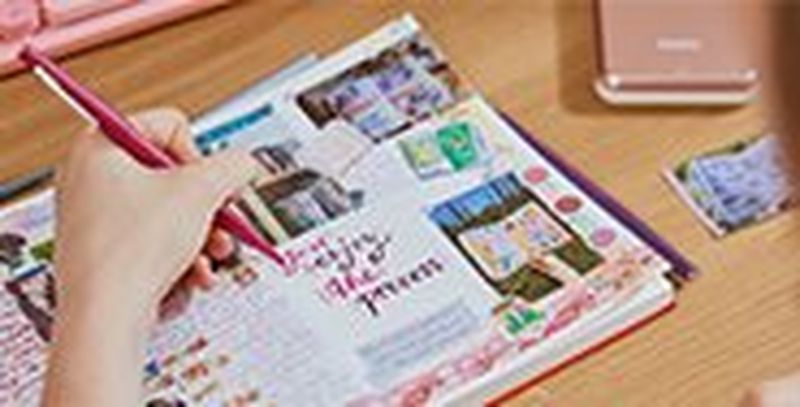 A person writing in a scrapbook, the pages filled with photos and stickers.