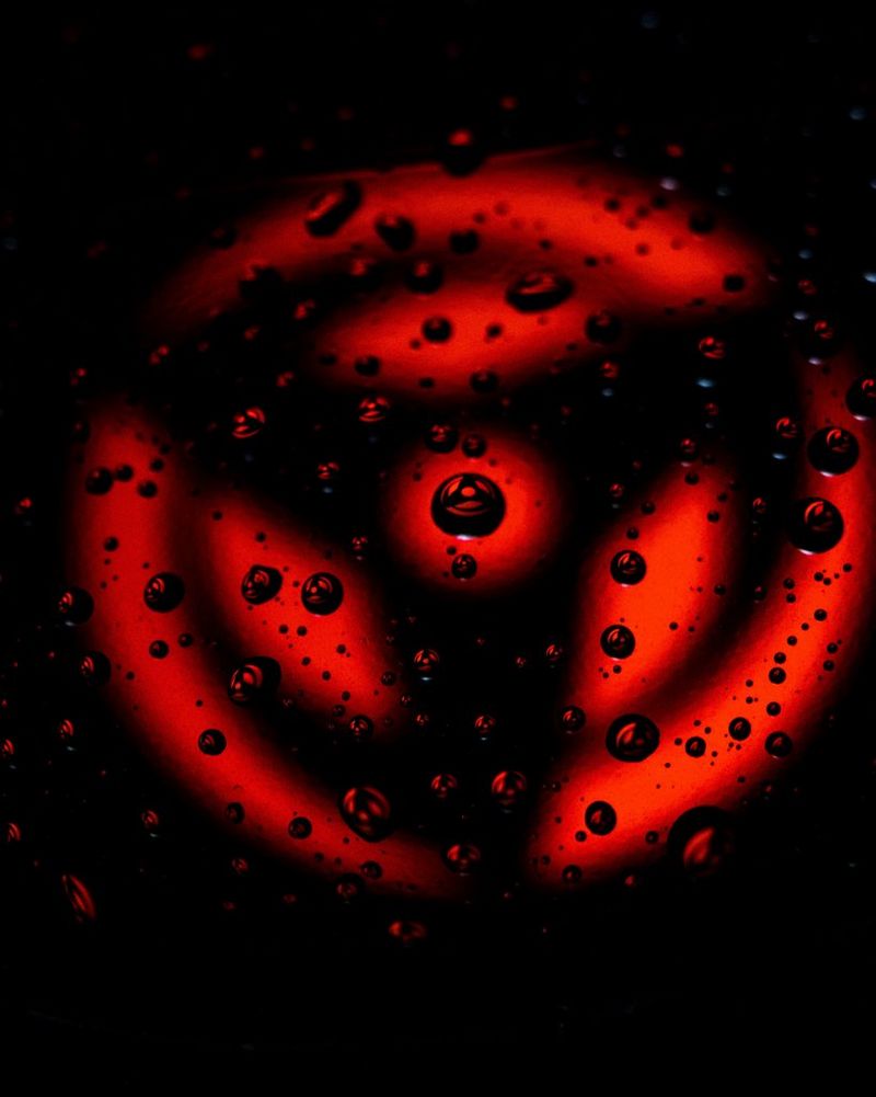 O formă circulară roşie cu trei spiţe care ies dintr-un punct central reflectat în picăturile de apă de deasupra sa.