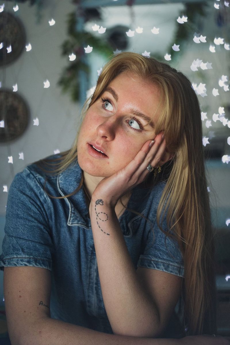 O femeie care priveşte în sus şi la dreapta ei, cu mâna pe obraz, cu luminiţe estompate, în formă de stea, în fundal.