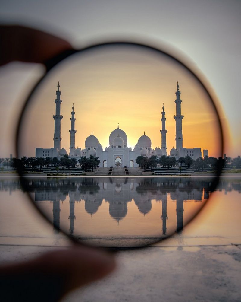 O structură de marmură albă cu peste o duzină de cupole şi patru minarete, privită printr-un inel în lumină aurie.