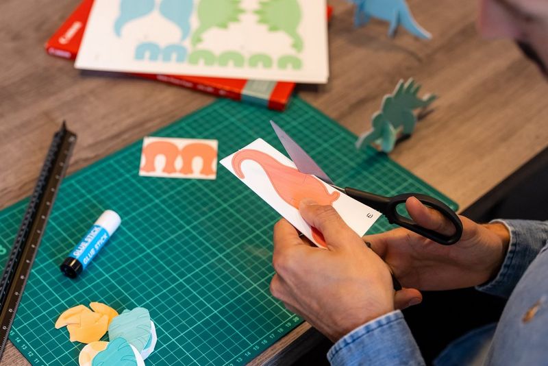 Мужчина вырезает изображение оранжевого динозавра для подвесного мобиля.